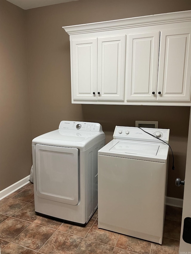 clothes washing area with cabinet space, baseboards, stone finish floor, and washing machine and dryer