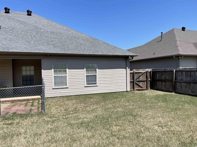 rear view of property featuring fence, a lawn, and roof with shingles