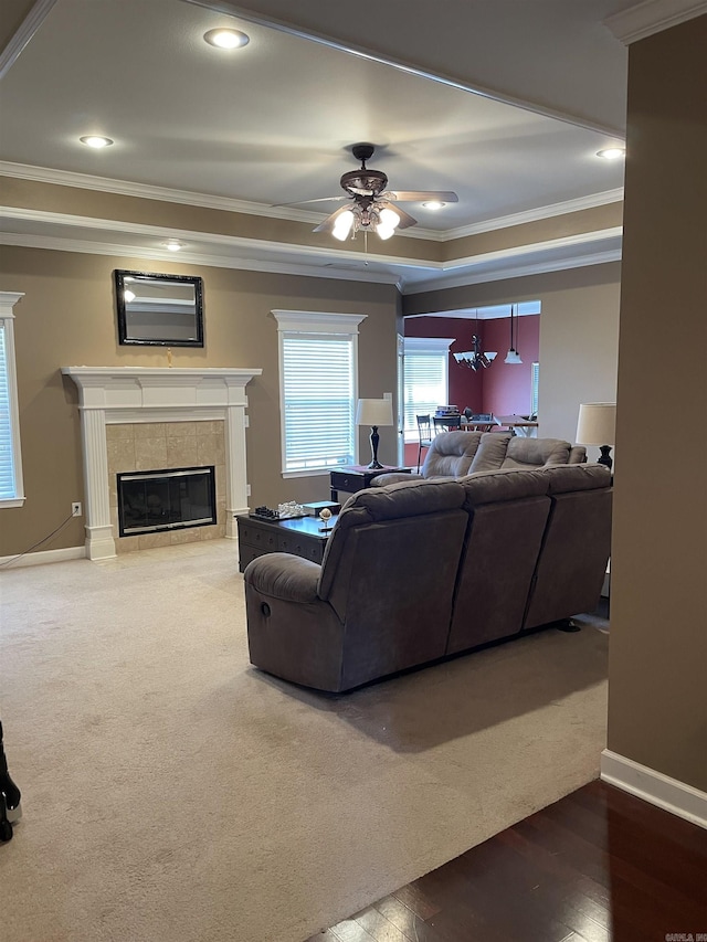 living area with crown molding, ceiling fan, a raised ceiling, and a tiled fireplace