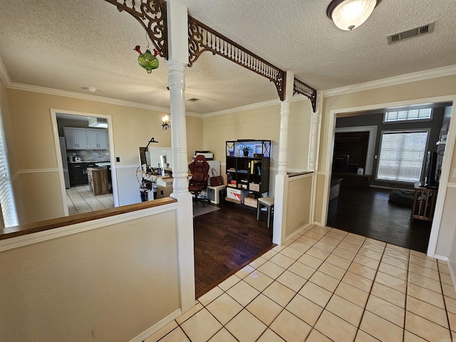 interior space featuring a textured ceiling, crown molding, light tile patterned flooring, visible vents, and decorative columns