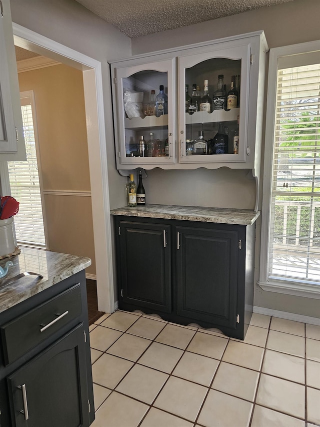 bar with light tile patterned floors, baseboards, crown molding, and a dry bar