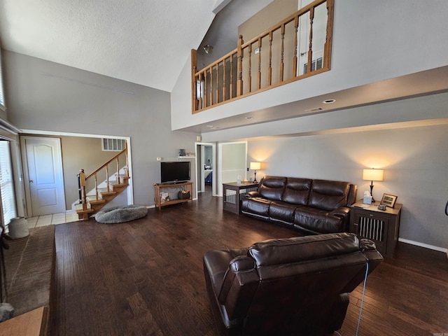 living area with high vaulted ceiling, visible vents, wood finished floors, stairs, and baseboards