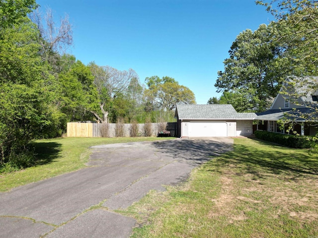 view of side of property featuring an attached garage, fence, a lawn, and aphalt driveway