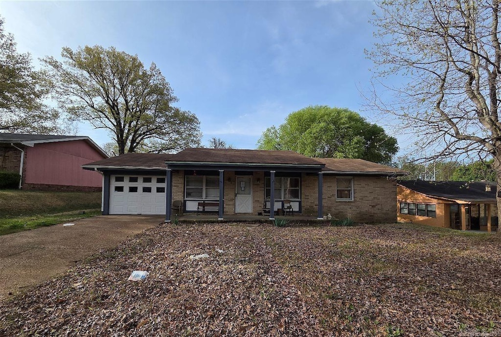 ranch-style house featuring brick siding, driveway, covered porch, and a garage