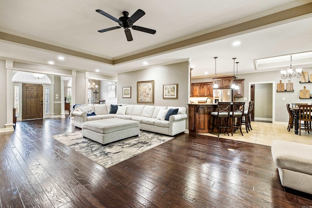 living area with crown molding, a tray ceiling, recessed lighting, ceiling fan with notable chandelier, and wood-type flooring