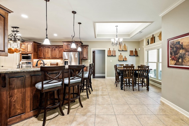 kitchen featuring a raised ceiling, a notable chandelier, ornamental molding, appliances with stainless steel finishes, and decorative backsplash