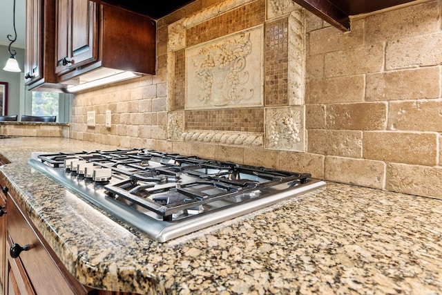 interior details with backsplash, stainless steel gas stovetop, and light stone counters