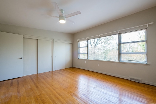 unfurnished bedroom featuring light wood finished floors, visible vents, multiple closets, and ceiling fan