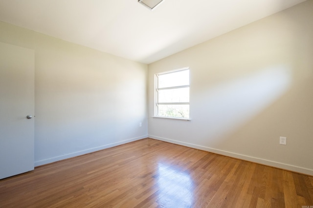 empty room with light wood-style flooring, baseboards, and lofted ceiling