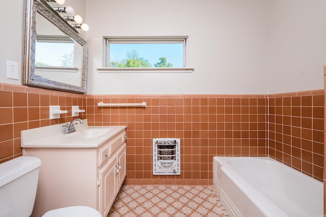full bathroom with a tub to relax in, vanity, toilet, wainscoting, and tile walls