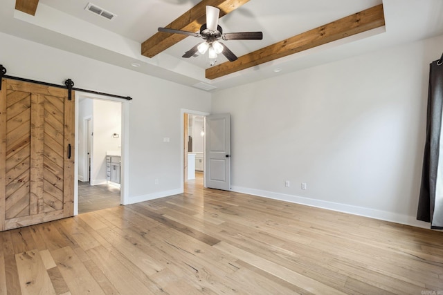 unfurnished bedroom with beamed ceiling, light wood-type flooring, visible vents, a barn door, and baseboards