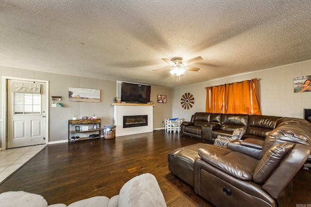 living room with a glass covered fireplace, wood-type flooring, a textured ceiling, and ceiling fan