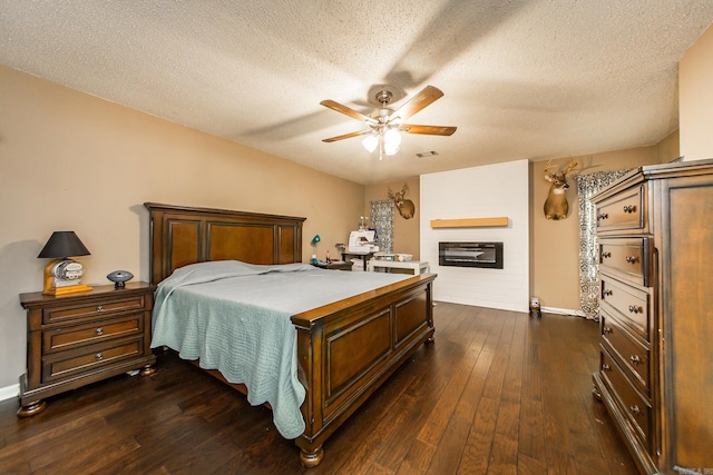 bedroom with a textured ceiling, a glass covered fireplace, dark wood-style floors, and visible vents