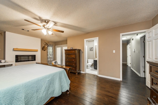 bedroom with a textured ceiling, a large fireplace, dark wood finished floors, and visible vents