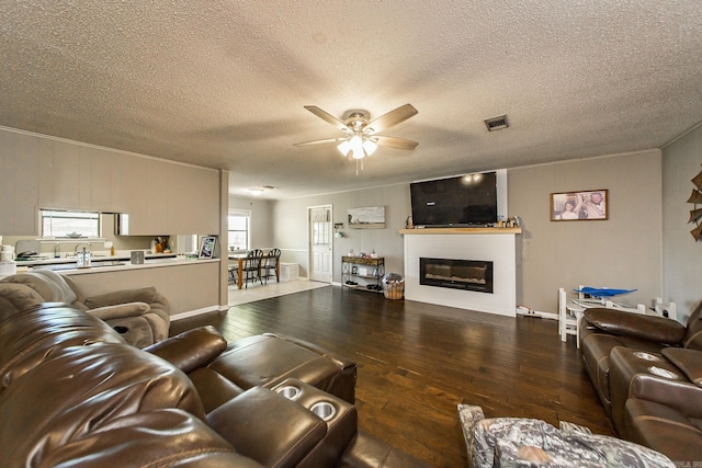living area featuring visible vents, ceiling fan, a textured ceiling, hardwood / wood-style floors, and a glass covered fireplace