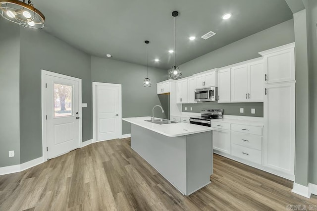 kitchen with appliances with stainless steel finishes, wood finished floors, a sink, and white cabinetry