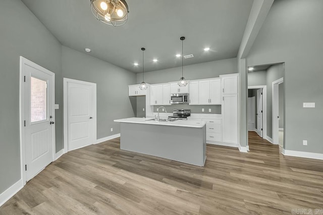 kitchen featuring stainless steel appliances, white cabinets, baseboards, and a center island with sink