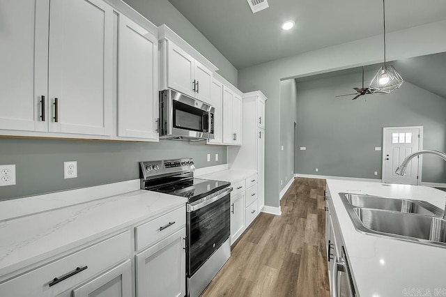 kitchen featuring light wood-style floors, pendant lighting, white cabinets, appliances with stainless steel finishes, and a sink