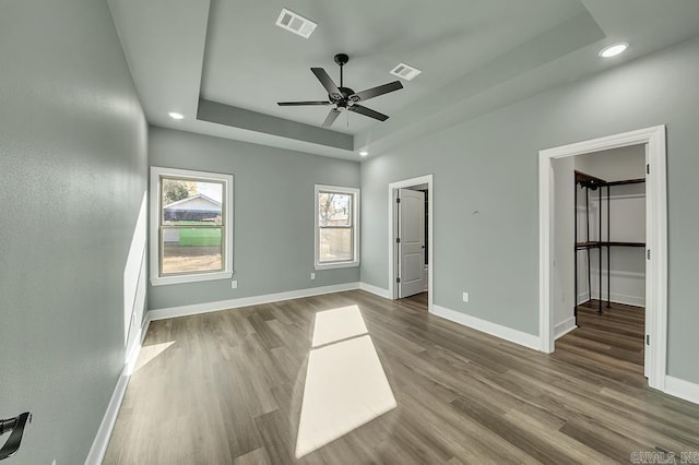 unfurnished bedroom with a tray ceiling, baseboards, and wood finished floors