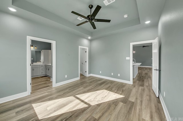 unfurnished bedroom with light wood-type flooring, a raised ceiling, recessed lighting, and baseboards