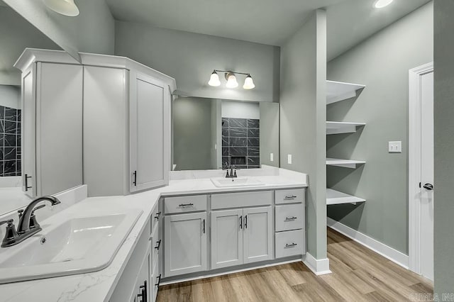 full bath with two vanities, baseboards, a sink, and wood finished floors