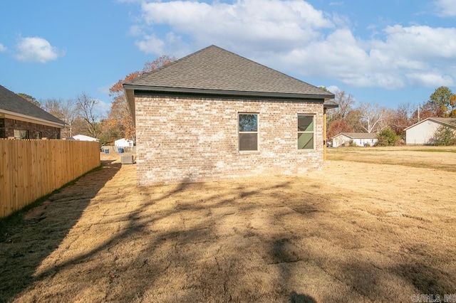 rear view of property with roof with shingles, brick siding, fence, and a lawn