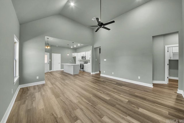 unfurnished living room with baseboards, a sink, ceiling fan, wood finished floors, and high vaulted ceiling