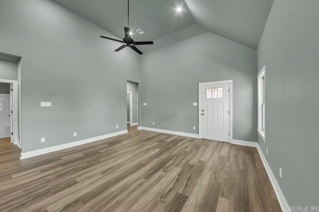 unfurnished living room with high vaulted ceiling, ceiling fan, visible vents, wood finished floors, and baseboards