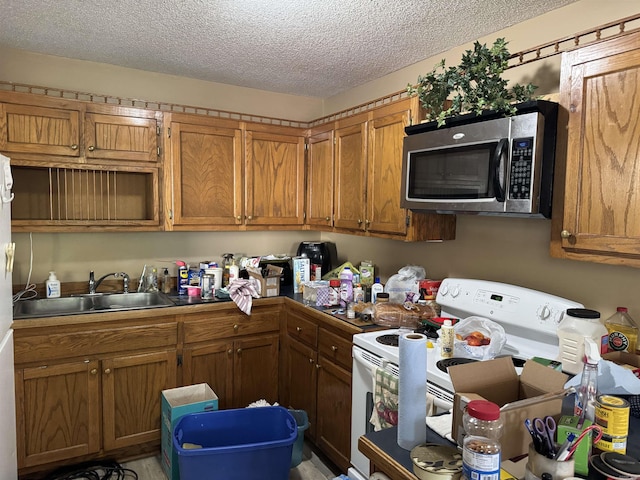 kitchen with stainless steel microwave, brown cabinetry, white electric stove, a sink, and a textured ceiling
