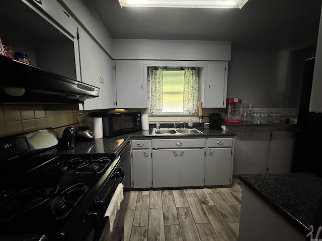 kitchen with light wood-type flooring, black appliances, a sink, dark countertops, and backsplash