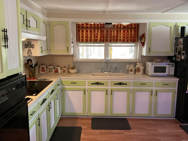 kitchen with a sink, light countertops, under cabinet range hood, black appliances, and wood finished floors
