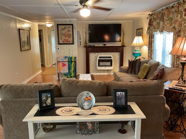 living room with baseboards, a brick fireplace, ceiling fan, heating unit, and wood finished floors