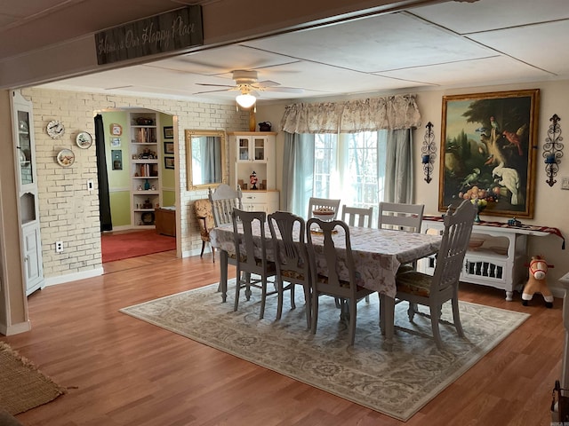 dining room featuring wood finished floors, ceiling fan, brick wall, and baseboards