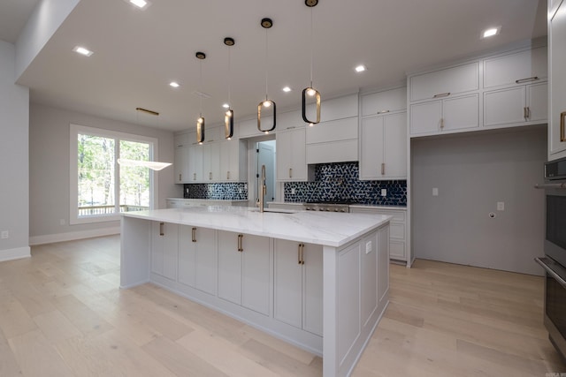 221 Abington Cir, Little Rock, AR 72223 - kitchen featuring a large island with sink, light stone countertops, decorative backsplash, white cabinetry, and light wood finished floors