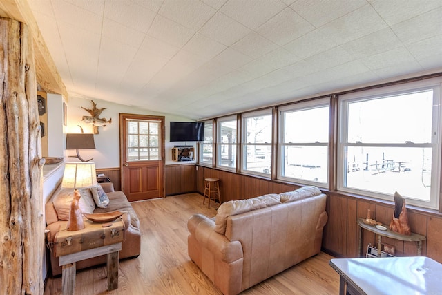 living area featuring light wood-style flooring, wooden walls, wainscoting, and lofted ceiling