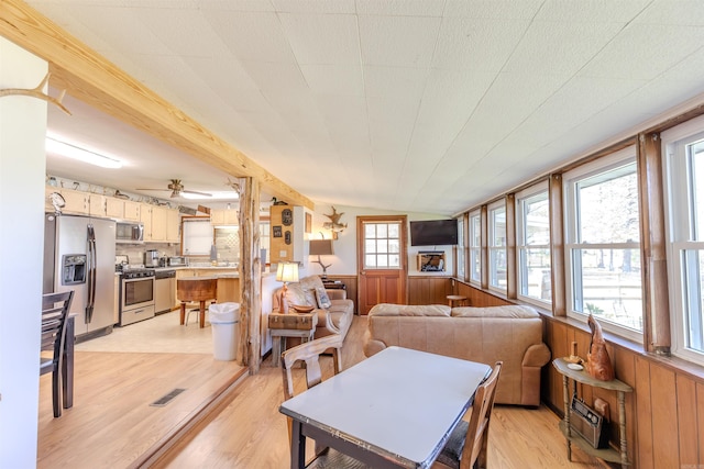 dining space featuring wood walls, light wood-style flooring, wainscoting, and visible vents