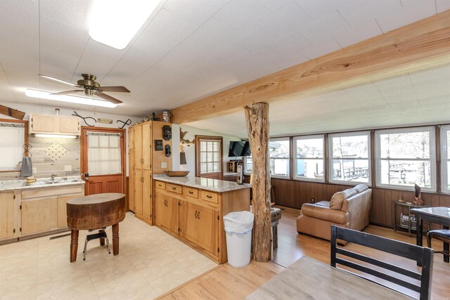 kitchen with ceiling fan, light floors, a peninsula, light stone counters, and a sink