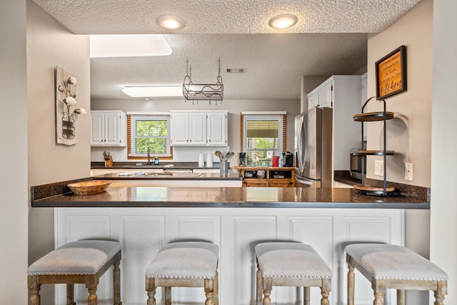 166 Heatherwood, Hot Springs, AR 71913 - kitchen featuring white cabinets, dark countertops, freestanding refrigerator, a peninsula, and a textured ceiling