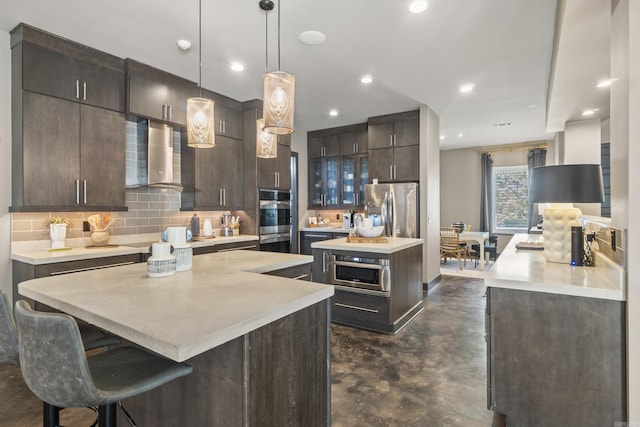 kitchen featuring finished concrete flooring, wall chimney exhaust hood, dark brown cabinets, appliances with stainless steel finishes, and a center island with sink