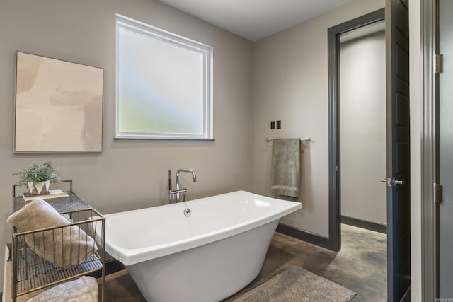 full bath featuring a freestanding tub, concrete flooring, and baseboards