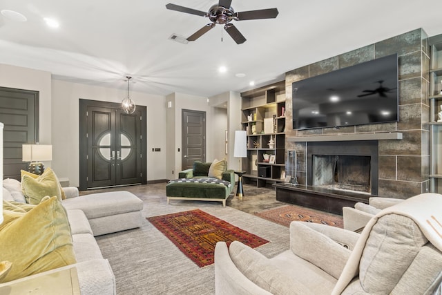living area featuring ceiling fan, visible vents, a tiled fireplace, baseboards, and built in shelves