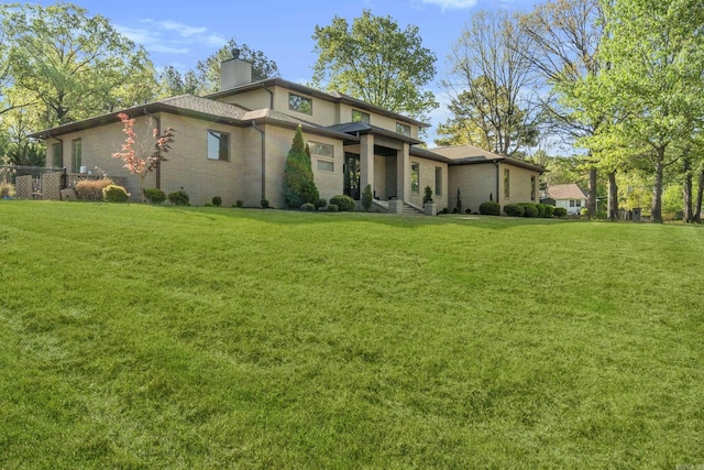 view of front of house featuring brick siding, a chimney, and a front lawn