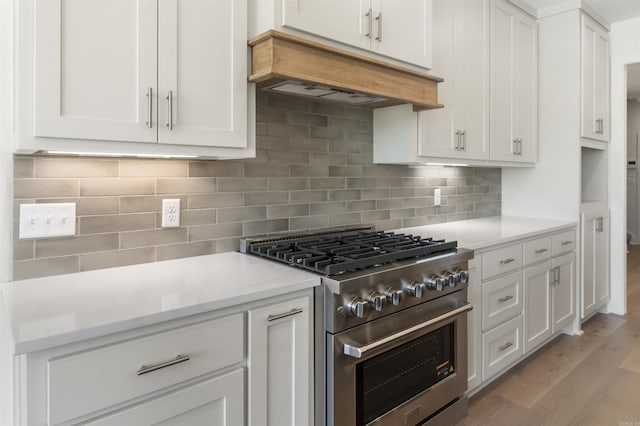 kitchen with white cabinets, stainless steel stove, under cabinet range hood, and light wood finished floors