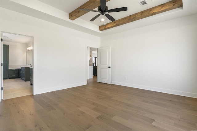 unfurnished bedroom featuring baseboards, ensuite bathroom, visible vents, beamed ceiling, and wood finished floors