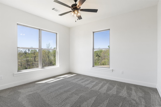 empty room featuring visible vents, baseboards, dark carpet, and a healthy amount of sunlight