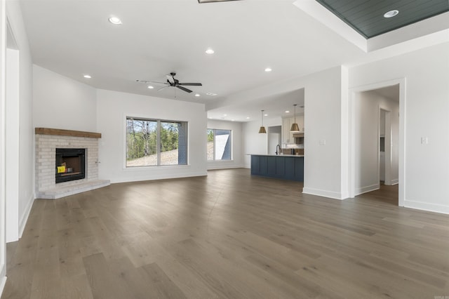unfurnished living room with baseboards, a brick fireplace, a ceiling fan, recessed lighting, and wood finished floors