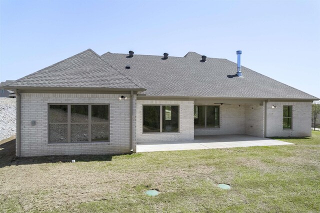 rear view of property with a shingled roof, a patio, brick siding, and a lawn