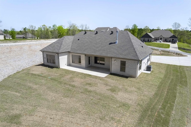 rear view of house with cooling unit, a lawn, roof with shingles, a patio area, and brick siding