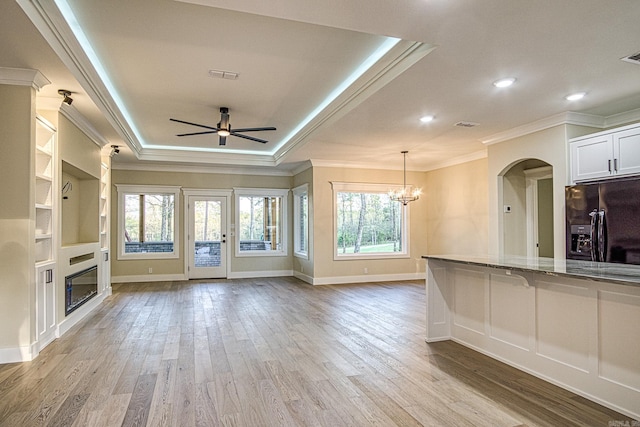 7 San Pablo Ln, Hot Springs Village, AR 71909 - unfurnished living room featuring a glass covered fireplace, crown molding, visible vents, a tray ceiling, and ceiling fan with notable chandelier