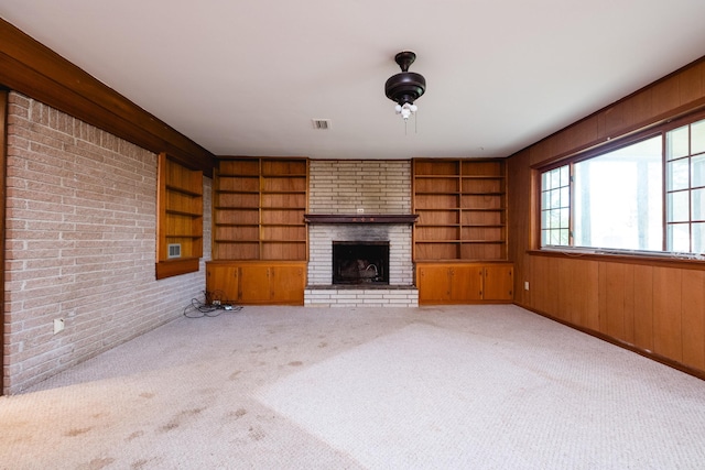 unfurnished living room with wooden walls, carpet floors, built in shelves, and a fireplace